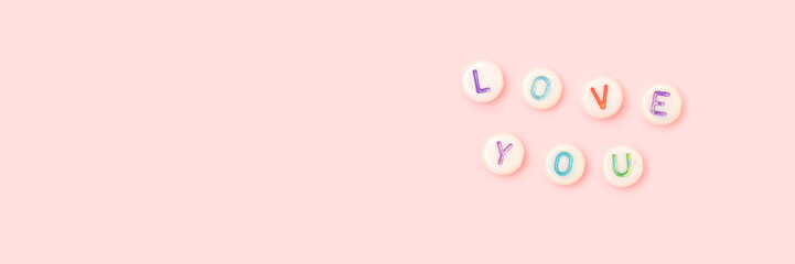 Love you. Banner with quote made of white round beads with colorful letters on a pink pastel background. Valentines Day concept.