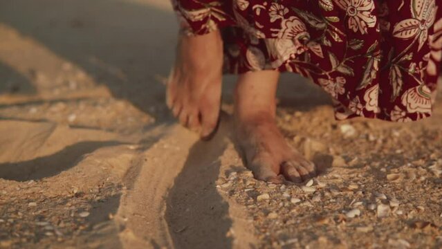 Close up shot of a woman in a dress pushing one foot backwards in the sand    