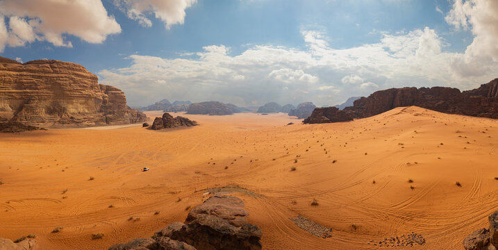 Panoramic view of Wadi Rum desert in Jordan with clouds moving over flat sand landscape with mountains in background, 