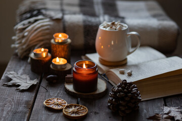Autumn cozy home composition with hot chocolate with marshmallow and candles. Aromatherapy on a grey fall morning, atmosphere of cosiness and relax. Wooden background, books, close up.