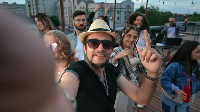 Happy hipster man blog vlog photo selfie at roof party discotheque dancing with friends crowd POV