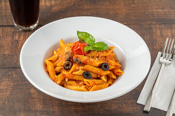 Penne pasta in tomato sauce, tomatoes decorated with parsley on a wooden background