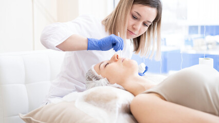 The cosmetologist applies the cream to the client's face in the beauty spa salon.