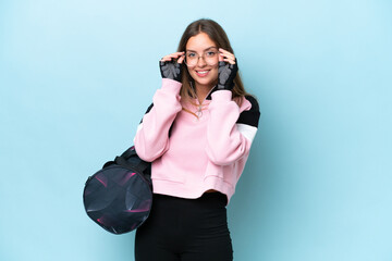 Young sport woman with sport bag isolated on blue background with glasses and surprised