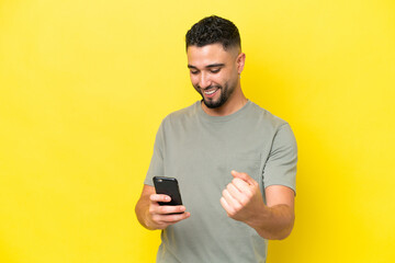 Young Arab handsome man isolated on yellow background with phone in victory position