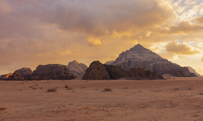 Fototapeta na wymiar Panoramic sunset view of Wadi Rum desert in Jordan with clouds moving over flat sand landscape with mountains in background, 