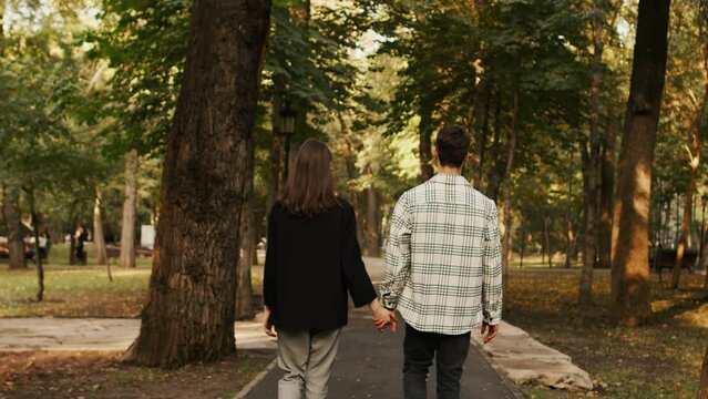 Unrecognizable man and woman, girlfriend and boyfriend holding hands while walking down the path in the nature park. Love, happiness, romantic relationship concept