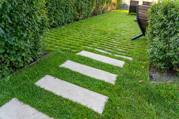 Green lawn and road surface from paving slabs in backyard. Gray color stepping tiles floor, strip...