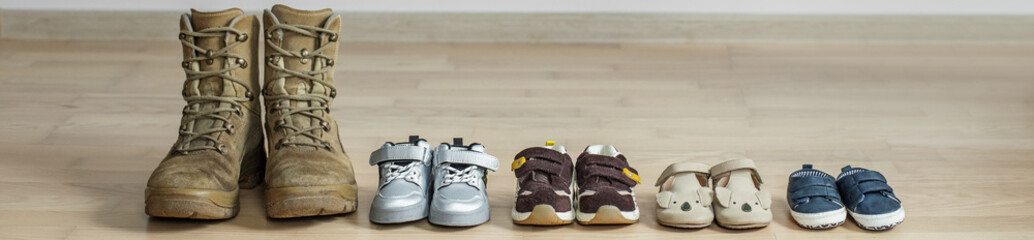 Old worn military boots and lot of baby shoes on wooden floor. Military father and family concept. © Olha Tsiplyar