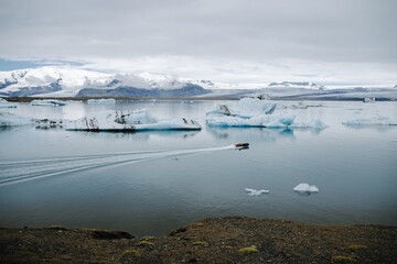 A boat with a man sails through the J&ouml;kuls&aacute;rl&oacute;n glacier lagoon in Iceland past icebergs that have broken away from the glacier tongue Brei&eth;amerkurj&ouml;kull. With a view of Hvannadalshn&uacute;kur.