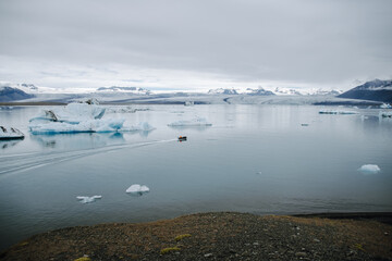 A boat with a man sails through the Jökulsárlón glacier lagoon in Iceland past icebergs that have broken away from the glacier tongue Breiðamerkurjökull. With a view of Hvannadalshnúkur.