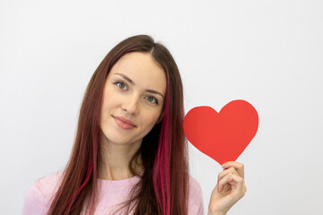 Beautiful young woman in love holding a red paper heart on a white background. The girl in pink looks straight at the camera and smiles
