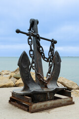 Fototapeta premium Admiralty anchor on pedestal on embankment of resort town. In background,turquoise December sea. Gelendzhik bay. Selective focus. Blurred background. Close-up. Gelendzhikk, Russia - December 13, 2022