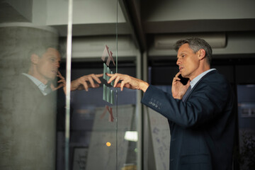 Portrait of successful businessman in office. Man writing ideas on colorful stickers on glass wall..