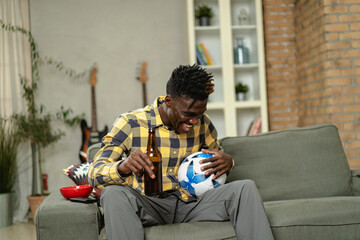 Young African man watching sport match on television and supporting his favorite team. Happy man enjoying victory, watching sports competition on tv.