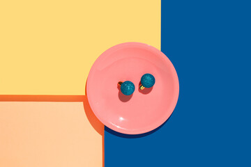 Minimal Holiday concept with blue Christmas balls in pink plate on a geometric background. Creative layout in blue, yellow and orange colors.