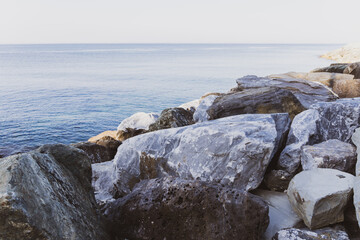 Close up of big stones of mediterranean sea shoe. Stone wave breakers of Italian coast on a sunny summer day. Genoa, region of Liguria, Italy.  Flat serene sea landscape.