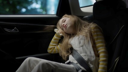 Fototapeta na wymiar Portrait of cute little tired girl sleeping on a back seat of a car
