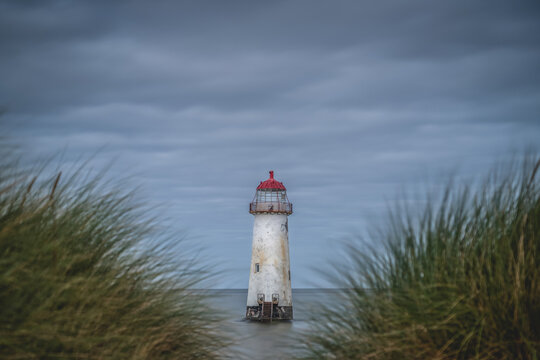 Lighthouse in a landscape photograph with blurred grasses in the foreground and a weathered battered lighthouse on a stormy day