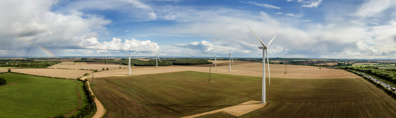Wind turbines, Aerial photograph of a wind farm showing wind turbines against a stormy backdrop and rainbow. generating green energy in all weathers