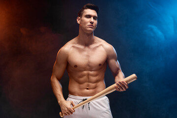 Strong and fit man bodybuilder with baseball bat posing with naked torso