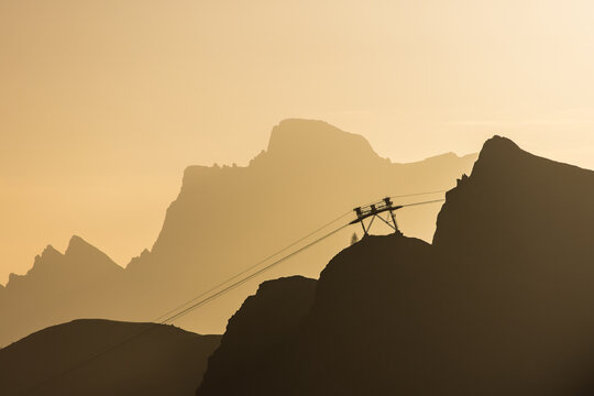 Silhouette of a gondola cableway up to a mountain during sunrise with the first sunbeams of the day in the Dolomites in Italy