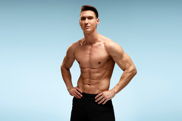 Young man bodybuilder showing his muscular body against blue background