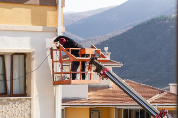 Worker without helmet repairing water pipe on crane, screw down with a drill