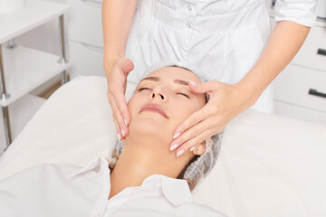 Cosmetologist massages woman face skin after rubbing moisturizing cream for rejuvenation, anti...