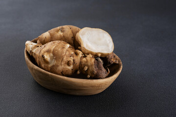 Jerusalem artichoke in a wooden bowl on a dark background.