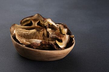 Dried Boletus edulis (king bolete) in a wooden bowl on a dark background.