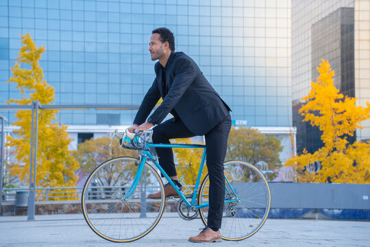 Handsome young stylish businessman going to work by bike. Riding a bicycle on city street near buildings