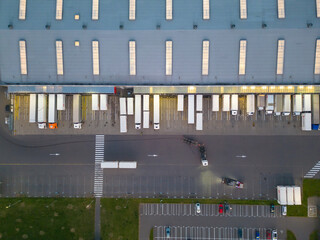 Aerial view of goods warehouse night. Logistics delivery; center in industrial city zone from above. Aerial view of trucks loading at logistic center. View from drone.