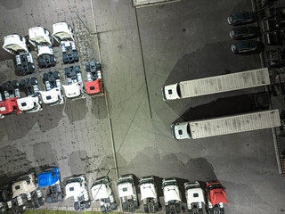 Aerial view of goods warehouse Night. Logistics center in industrial city zone from above. Aerial view of trucks loading at logistic center