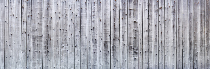 Graue verwitterte Panorama Holzwand aus senkrechten, unterschiedlich breiten Brettern mit starker Maserung