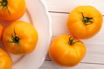 Several natural yellow tomatoes with a white plate, close-up, on a wooden table, top view.
