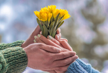 Young loving couple holding hands each other with bouquet of yellow flowers in summer park, view of hands