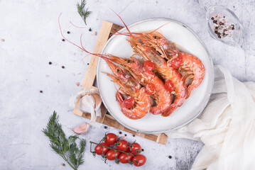 Baked langoustines in garlic sauce with cherry tomatoes on a white plate on a marble background, side view.