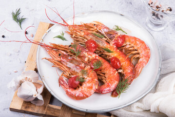 Baked langoustines in garlic sauce with cherry tomatoes on a white plate on a marble background, side view.