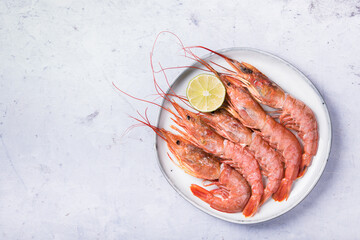 Langoustines on a white plate with lime on a light marble table, top view.