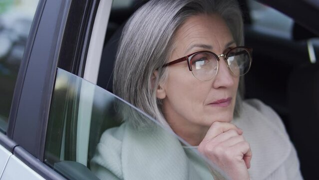 Self-confident senior business woman looking car window, watching over employees