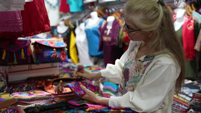 Mature woman tourist wearing ethnic clothes shopping for purse in a souvenir shop in Merida, Yucatan, Mexico.