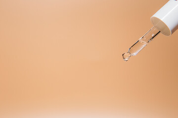 Cosmetic pipette with a yellow oily serum close up on beige background