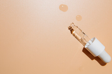 close up of pipette with pouring liquid serum and shadows on beige background. Trendy cosmetics shot with hard shadows.