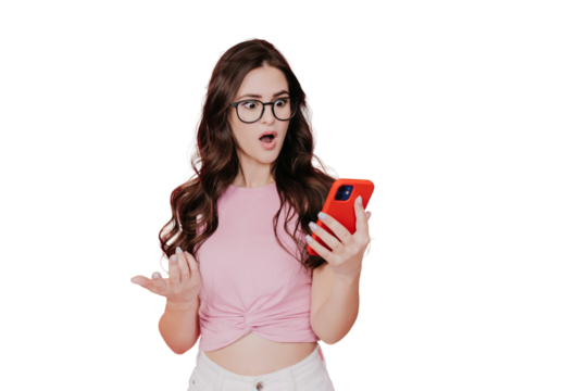 Amazed young brunette hispanic woman with wavy long hair looks at phone with wide opened eyes and mouth in surprise, standing against pink transparent background. Girl in glasses shocked, sale. Mockup