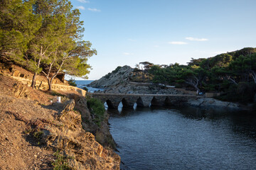 Fototapeta na wymiar Puente hacia una isla en el pueblo de la Costa Brava de Cadaqués rodeada del azul mar Mediterráneo con el sol bañándolo todo.