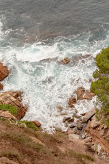 Obraz premium La espuma del mar Mediterráneo formándose al romper las olas contra las rocas de los acantilado de las murallas del pueblo catalan Tossa de Mar.