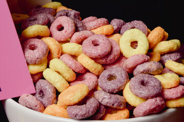 Cereales de colores con sabor a frutas saliendo directamente de la caja al bol de cerámica para que pueda desayunar un niño.