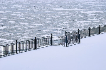 Snowfall on the embankment of the Amur River during ice drift. Black metal railings. Stair railing covered with snow. No people. Blagoveshchensk, Far East, Russia.