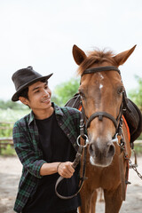 Fototapeta premium asian man in cowboy hat leads the horse's head on the leash at the ranch